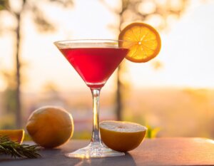 Cosmopolitan cocktail shining in the golden hour sunlight with lemon and rosemary